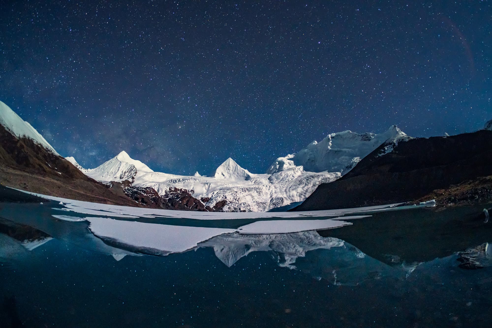 Montagnes enneigées sous la Voie lactée, reflétées à la surface de l’eau.