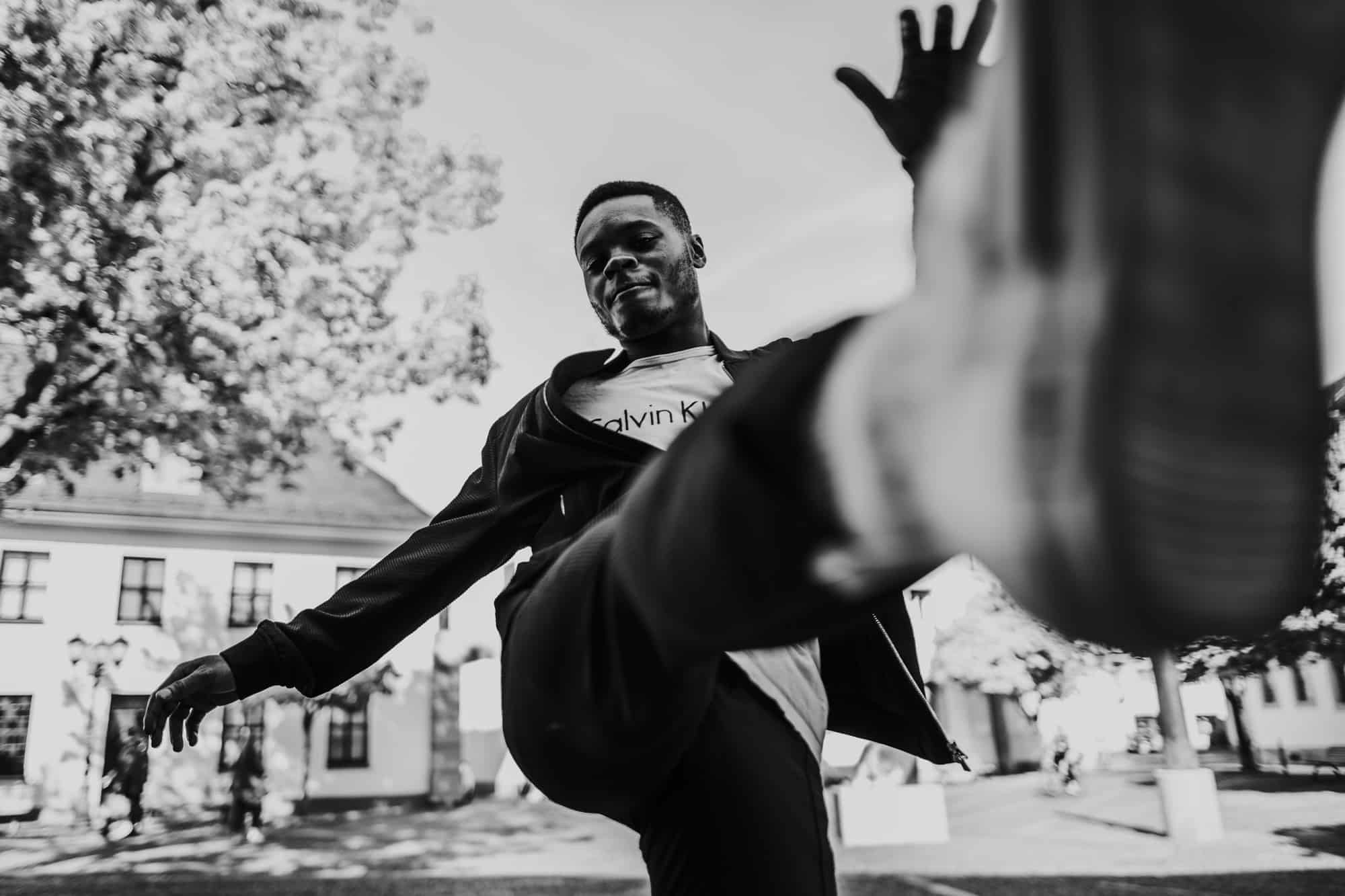 Dynamic black-and-white urban street photography with a man kicking toward the camera and strong visual depth.