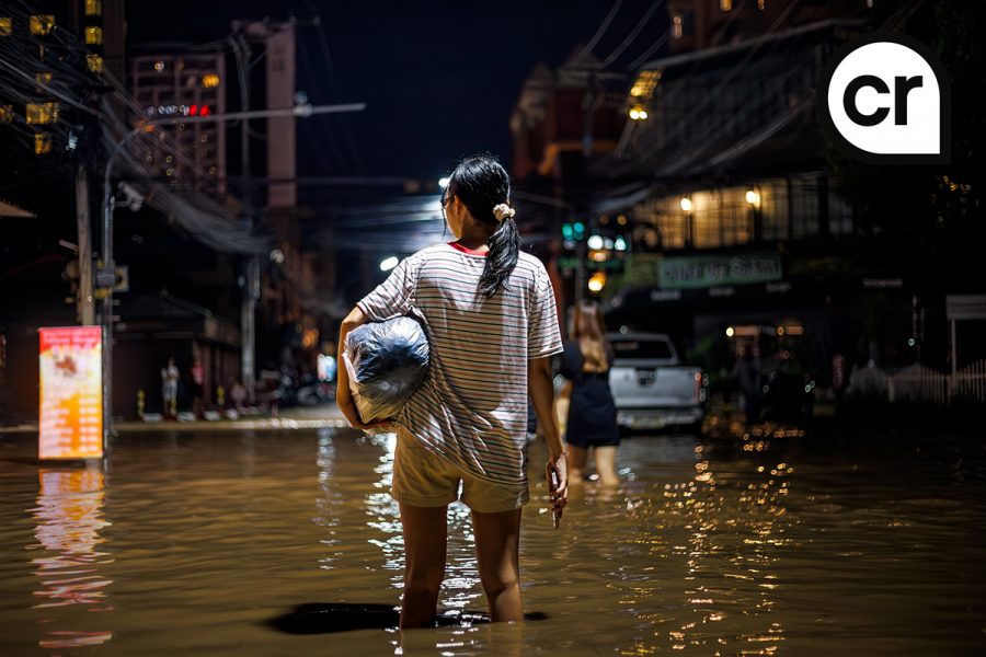 flood victims woman stands in the flooded streets of Chiang Mai city at night 2024, holding a bag with personal belongings. Another person wades ahead through the water