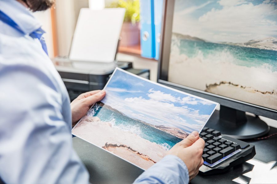 The,Graphic,Designer,Compares,The,Printed,Photo,With,The,View The graphic designer compares the printed photo with the view on the monitor