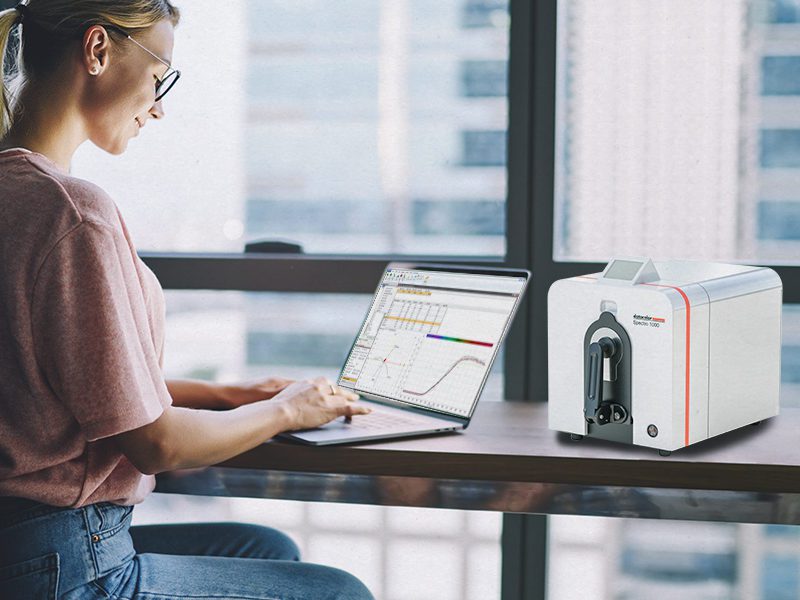 Woman seated at a table working on a laptop next to a Datacolor Spectro 1000.